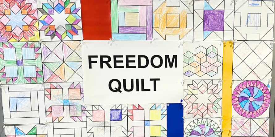 Quilt patterns coloured by children are taped to a wall making a Freedom Quilt.