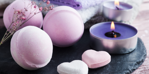 A picture of a lit purple candle and pink bath bombs