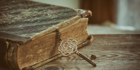 aged book with an old key attached to it on a wooden table