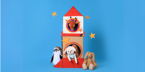 A cardboard rocket ship with stuffed animals inside.
