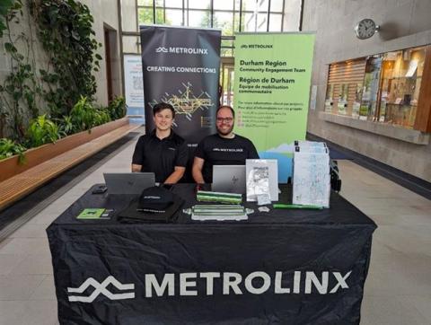 Two Metrolinx staff members sitting at a small information table with flyers on the table.