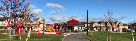 a suburban park with trees, play equipment, gazebo and houses in the background