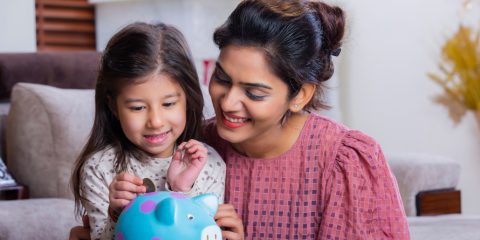 Mother and daughter adding coin to piggybank. 