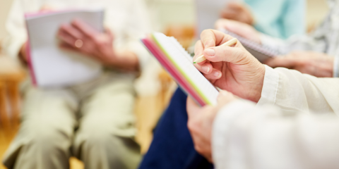 Person writing in a notebook with others behind them doing the same.