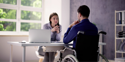 Man in wheelchair speaking with woman behind desk.