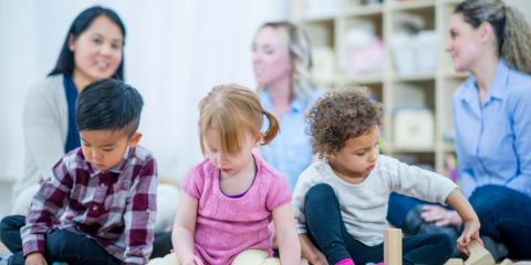 Children playing with blocks, their parents behind them, talking. 