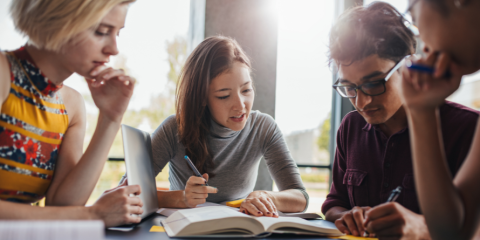Group of people around a table, speaking with each other, books open on the table.