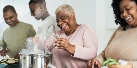 Four people smiling while cooking together in a kitchen. 