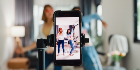 Two girls filming a video on a phone. 