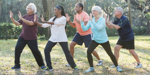 Five adults performing tai chi in the park. 