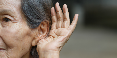 Senior woman with a hand cupped behind her ear. 