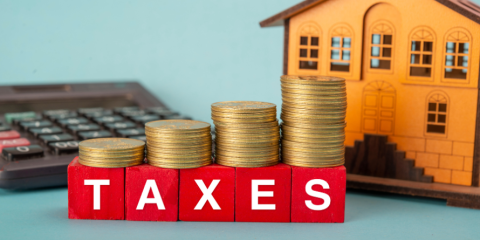 Calculator, blocks that spell "taxes' with coins stacked atop, miniature house. 