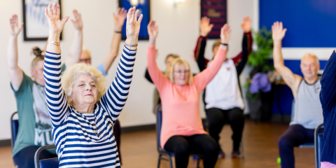 Seniors sitting in chairs with their arms extended. 