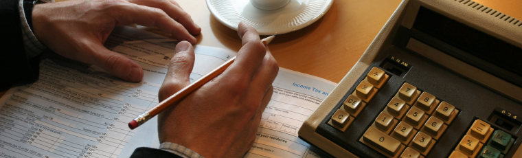 hands resting on a table with tax forms, coffee and calculator, hand are holding a pencil