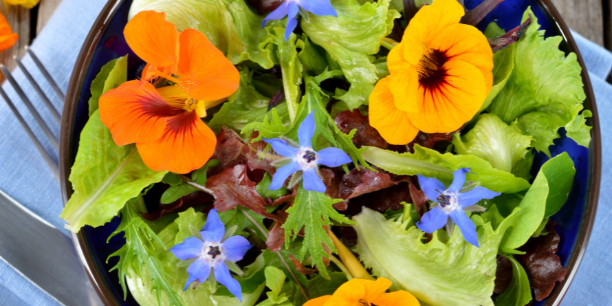 lettuce and flowers in a bowl with a fork beside the bowl