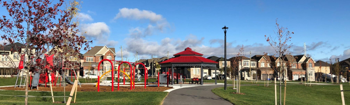 a suburban park with trees, play equipment, gazebo and houses in the background