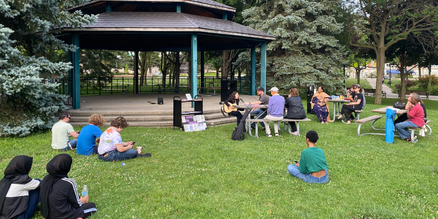 Group of people seated on the grass at the foot of a gazebo.
