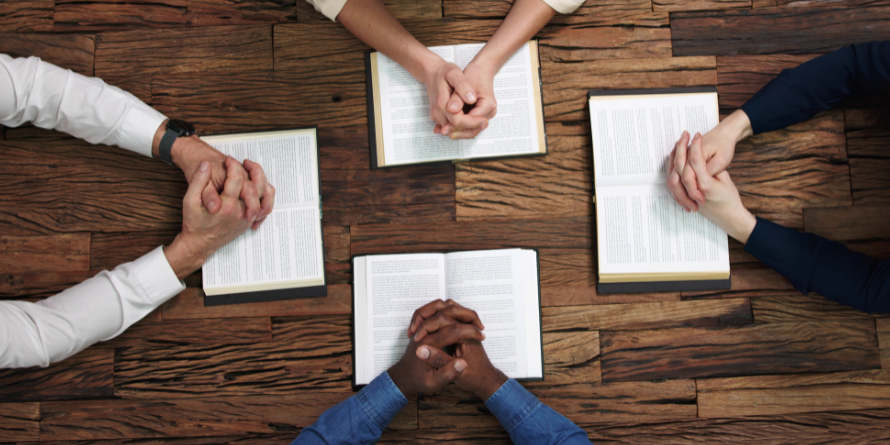 Four people with their hands crossed with open books in front of them.