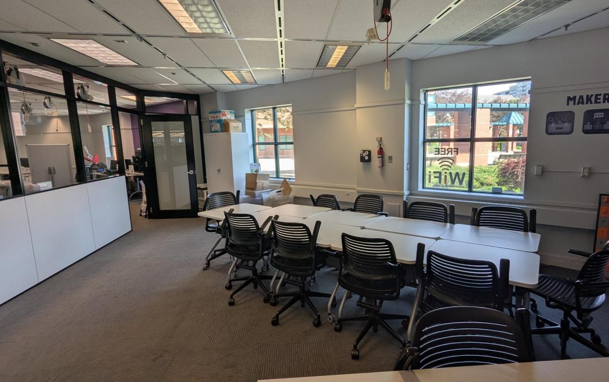 Picture of Event Room with 9 desks and chairs and an open door.