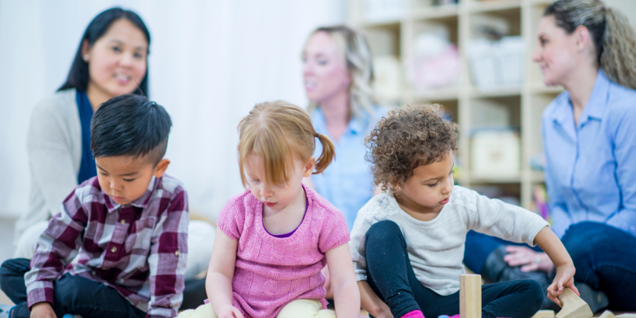 Children playing with blocks, their parents behind them, talking. 