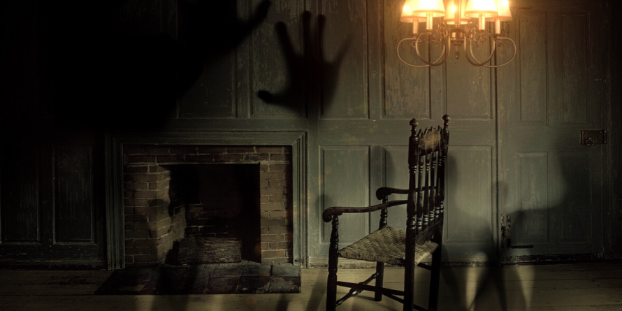 Dark fireplace, rocking chair, shadowy hand print on the wall.