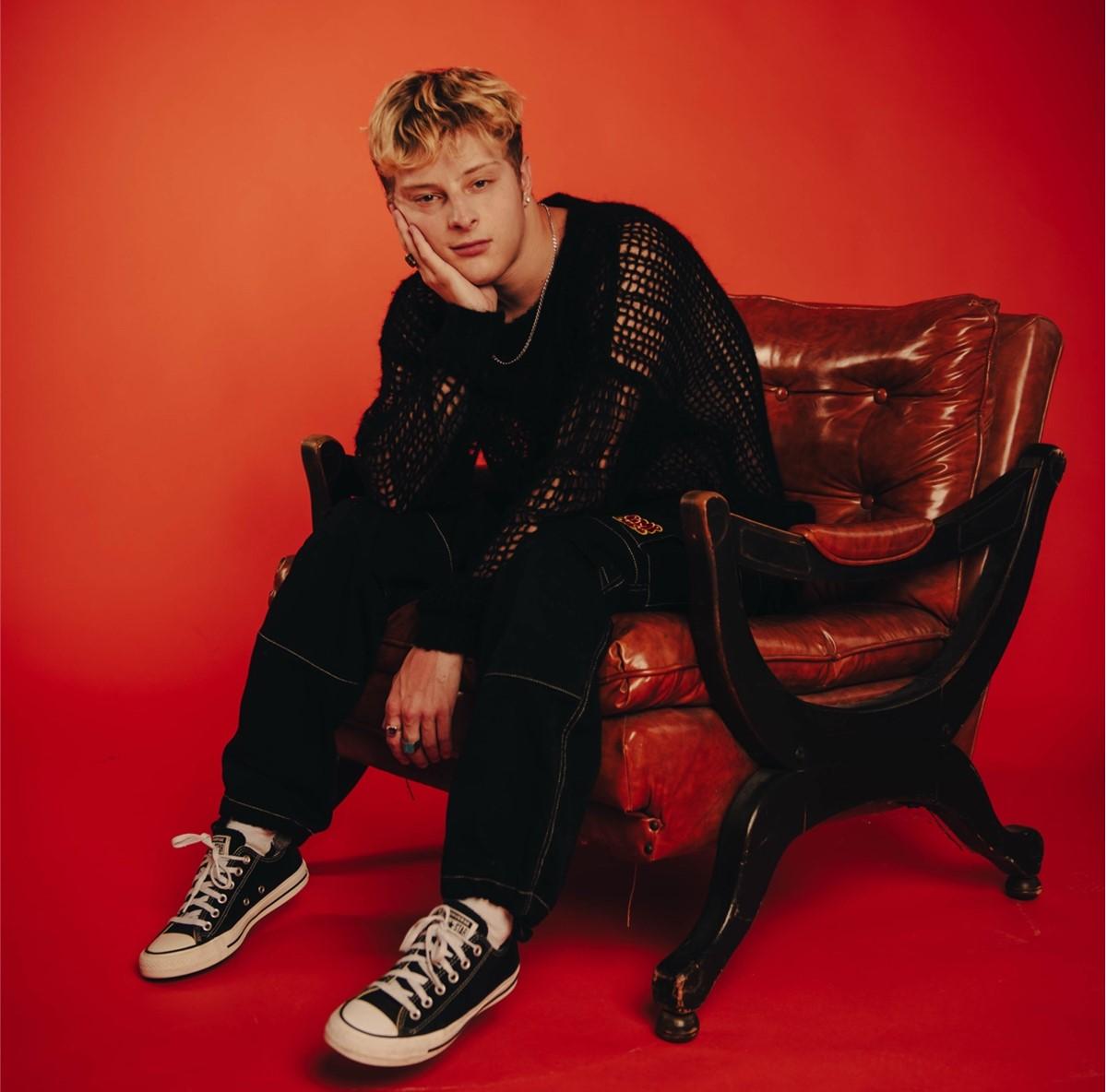 Joseph Robinson sitting in a chair infront of a red background