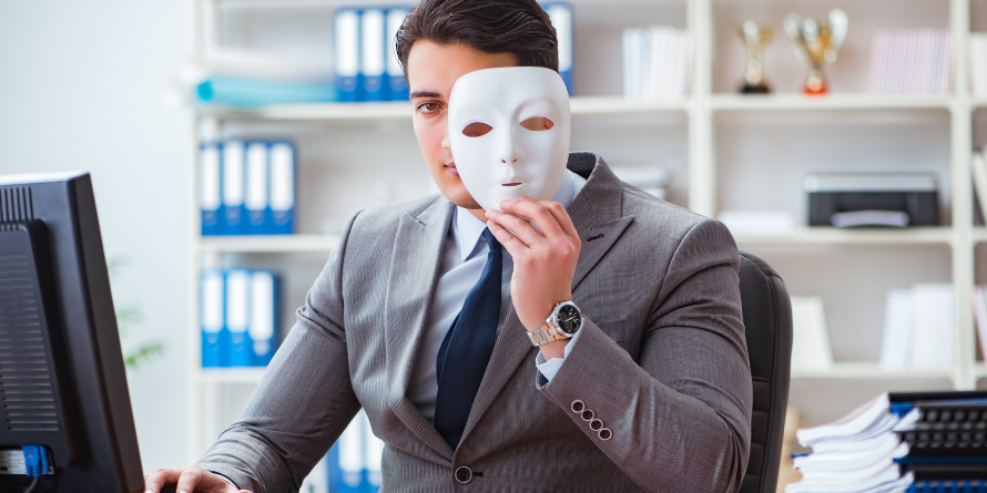 Man on a computer, peeking behind a blank mask. 