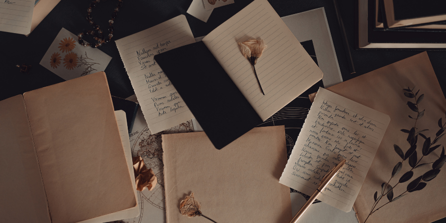 Open books, pens, writing, strewn across a table. 