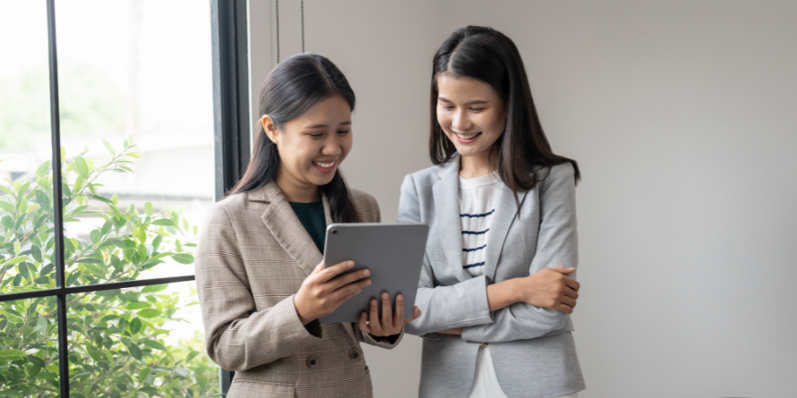 Two women smiling, one holds a tablet.