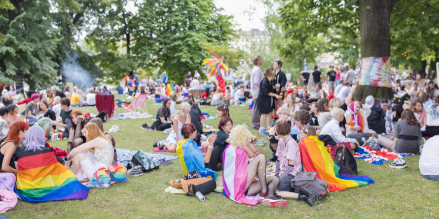 Many people seated on the grass outside with pride flags draped over their shoulders. 
