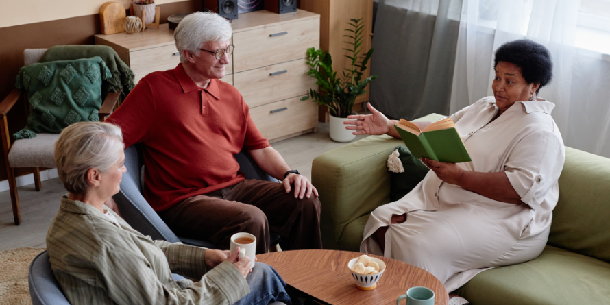 Three people seated around a table, one with a book in hand.