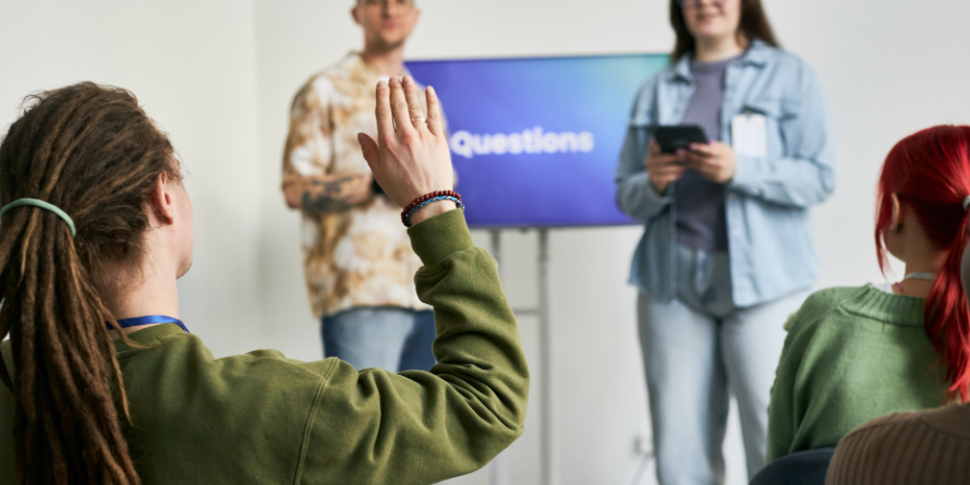 Two people hosting a presentation with a television, two people in the audience. 